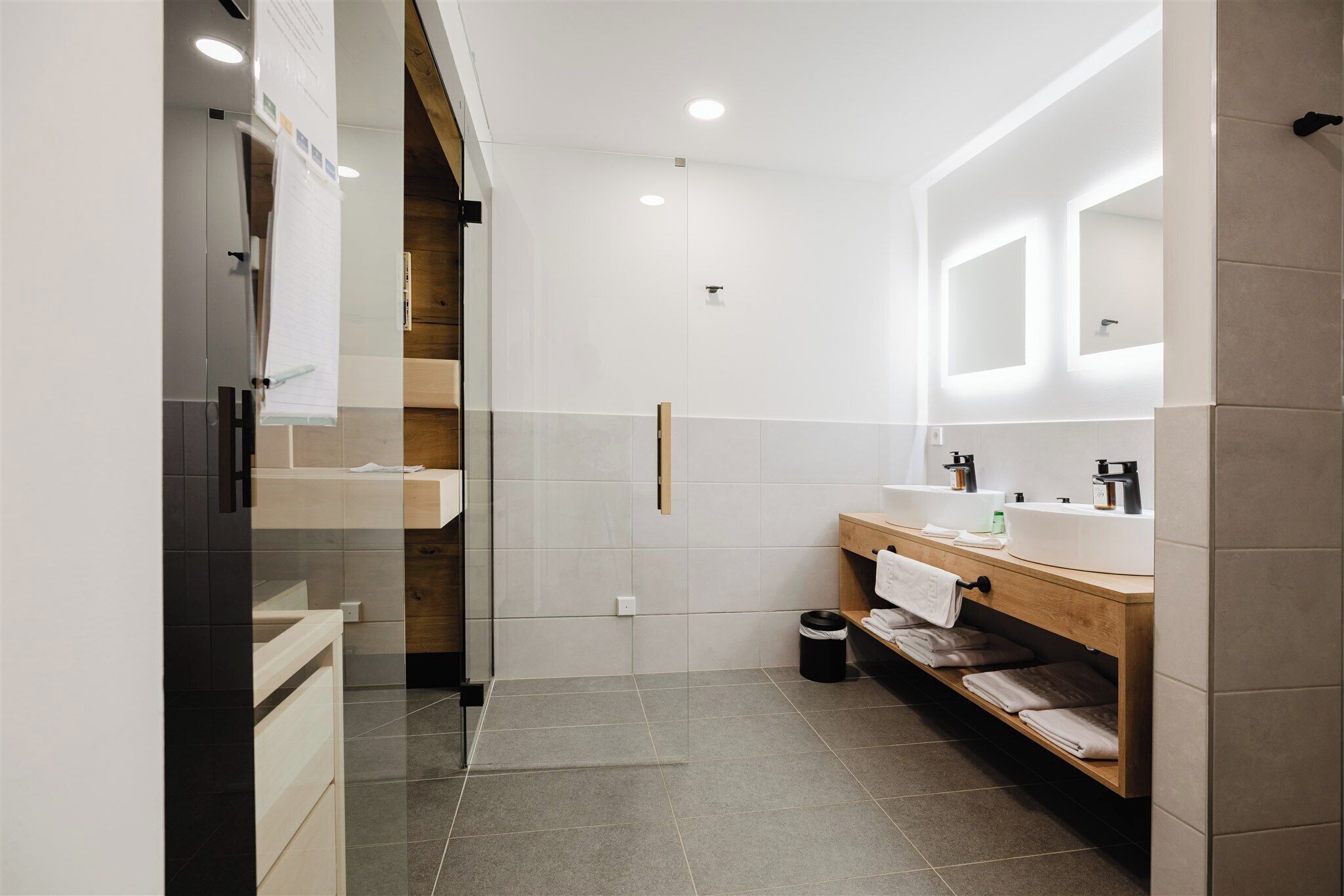 Une salle de bain moderne avec une paroi en verre, un meuble-lavabo en bois et un grand miroir.