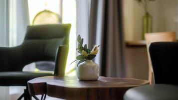 Una habitación con una mesa redonda de madera, un sillón verde y un jarrón blanco con una planta.