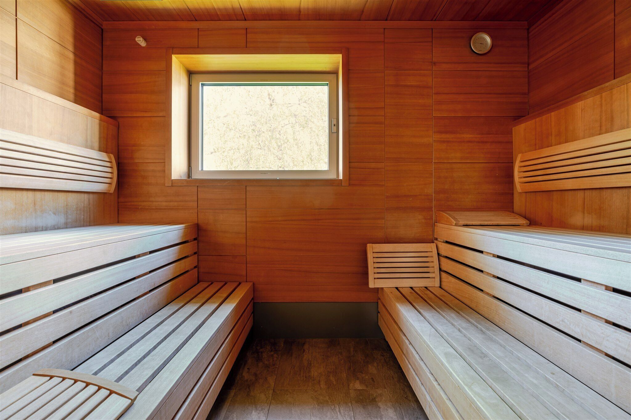 A sauna with wooden benches, a small window, and a wooden ceiling.