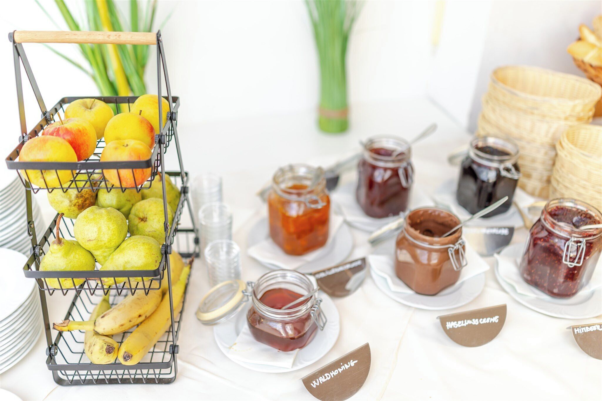 Un panier de fruits contenant des pommes et des poires, entouré de pots de confitures sur une table.