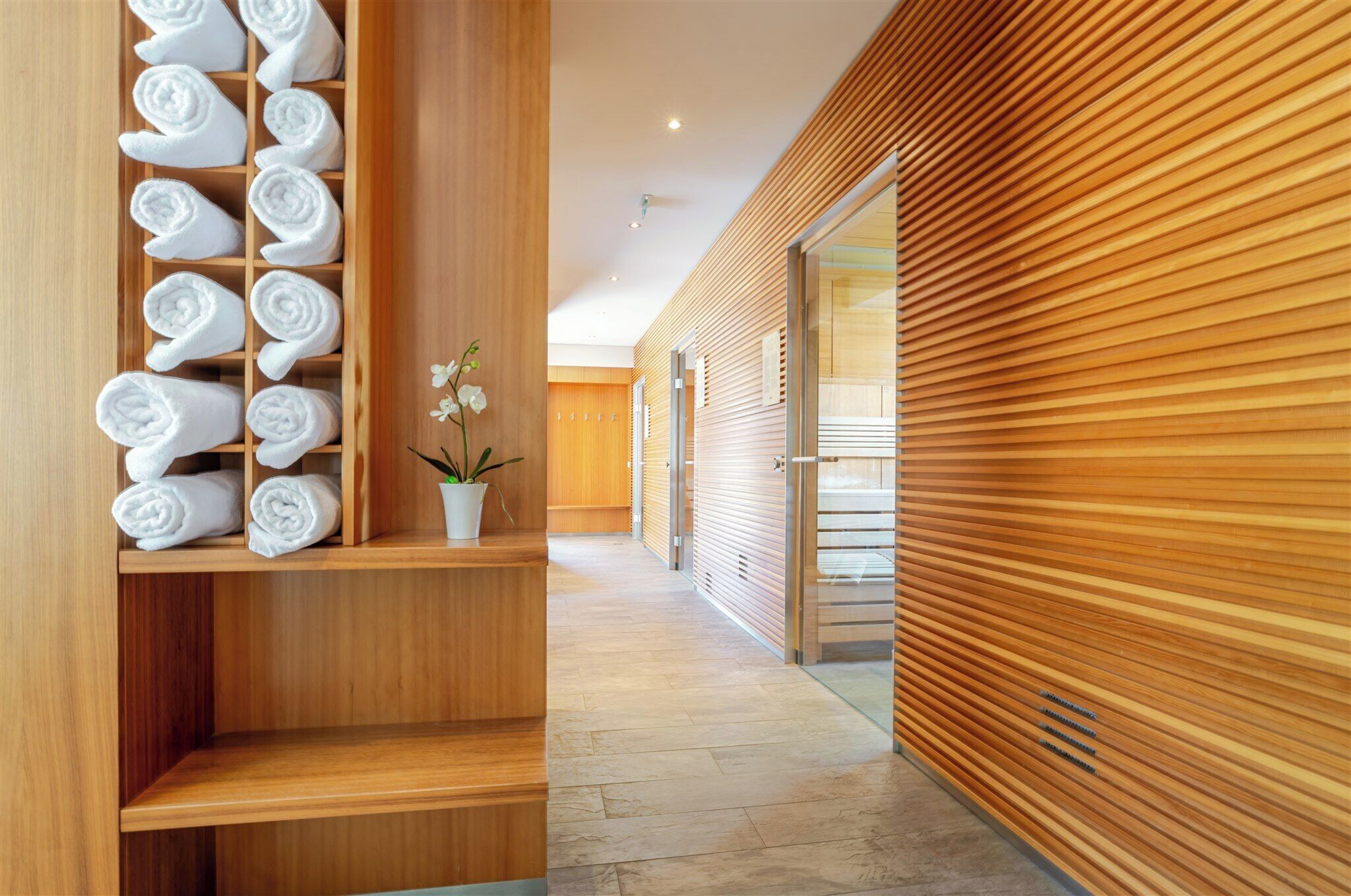 Un corridoio con pareti in legno, un portasacchi con asciugamani ordinatamente piegati e un'orchidea in vaso.