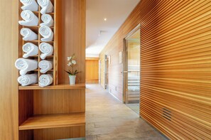 A hallway with wooden walls, a towel rack with neatly rolled towels, and a potted orchid.