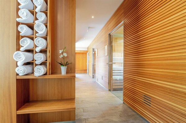 A hallway with wooden walls, a towel rack with neatly rolled towels, and a potted orchid.