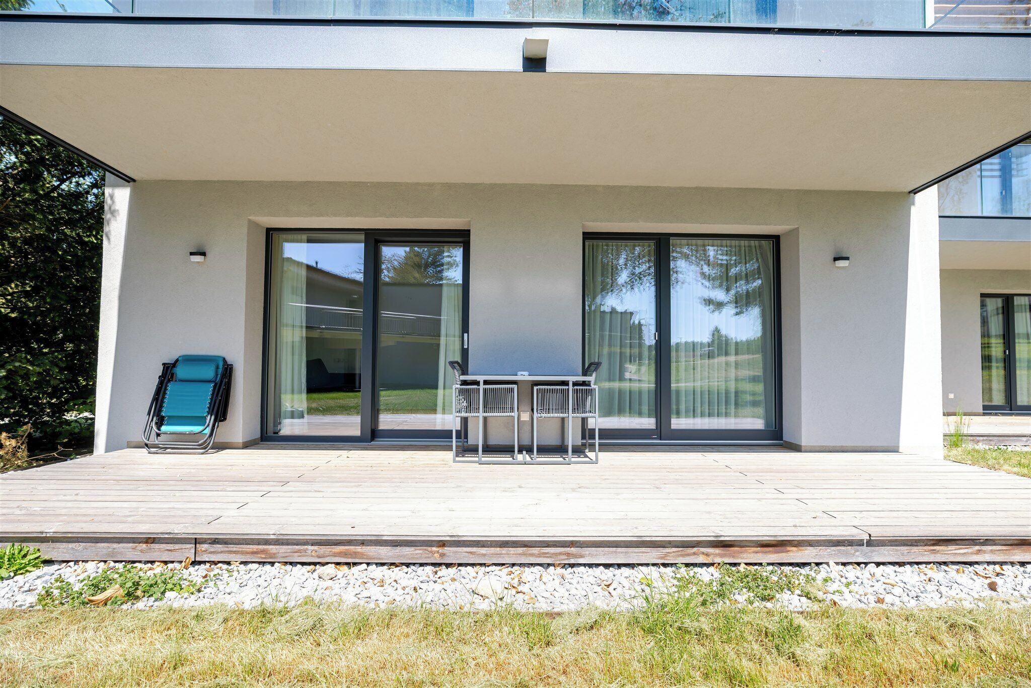 A modern building with a covered patio area, a table with chairs, and a blue chair.