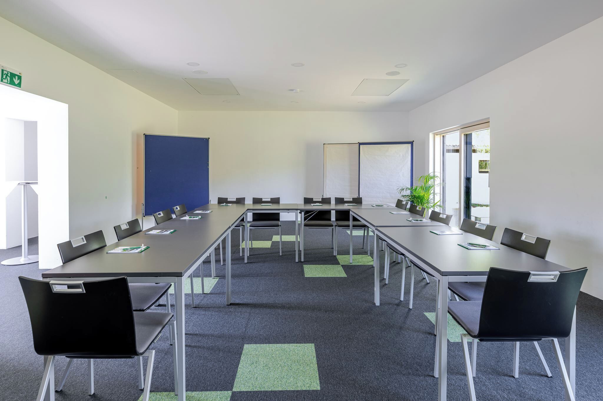 Uma sala de conferência com uma mesa comprida, cadeiras, um quadro branco e uma planta.