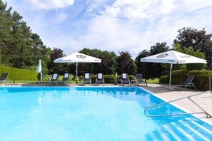 A swimming pool with lounge chairs and umbrellas, surrounded by greenery.
