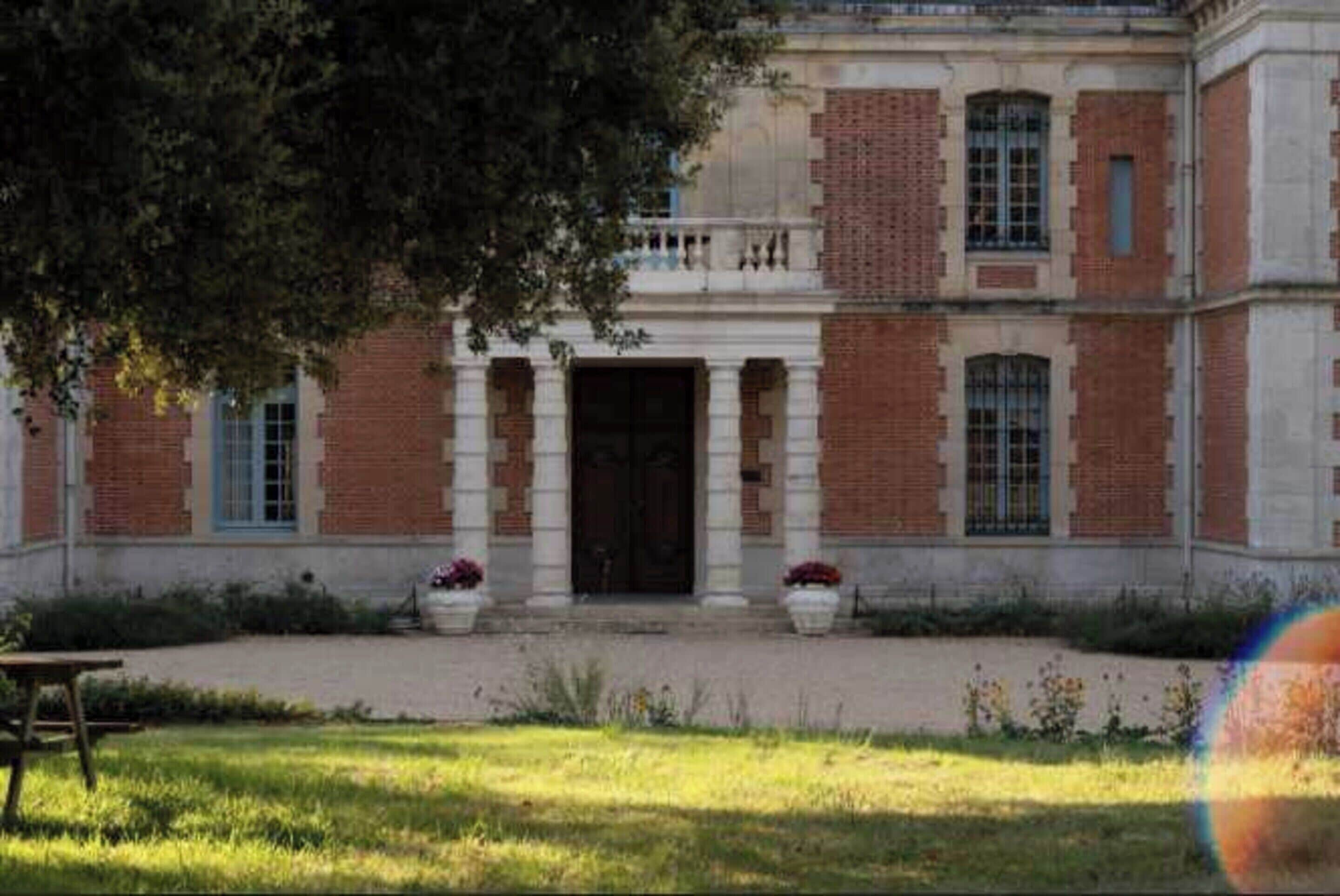 Un bâtiment à la façade symétrique, doté d’une entrée centrale encadrée de colonnes, et flanqué de fenêtres et de murs en briques.