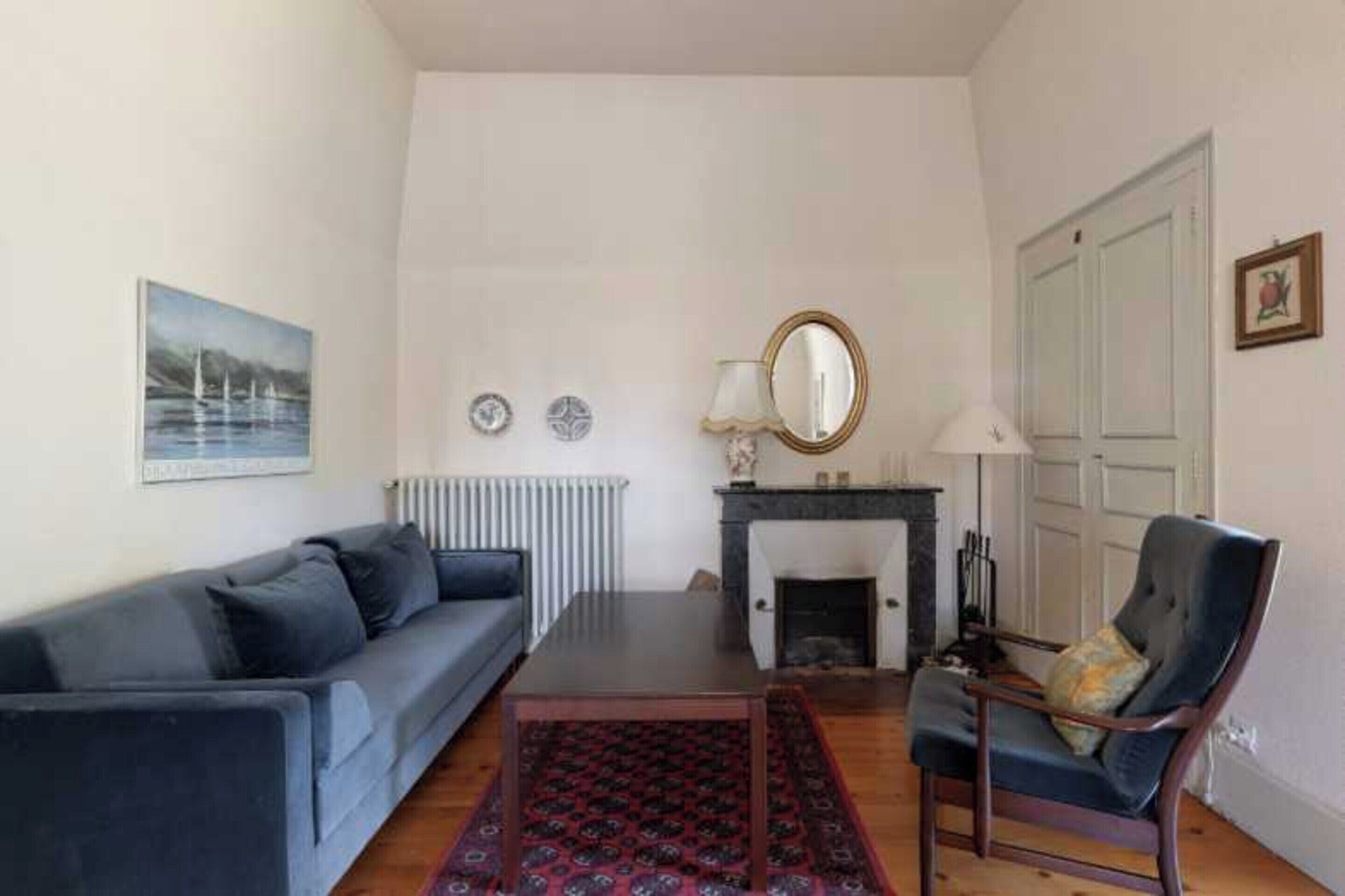 Un salon comprenant un canapé, un fauteuil, une cheminée, un radiateur et un tableau encadré accroché au mur.