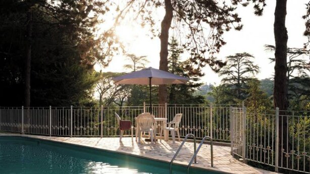 A swimming pool with a fenced deck, surrounded by trees and a patio area with chairs and an umbrella. - Chateau Stay - 1br/4p With Pool & Park Access (Fajolles)