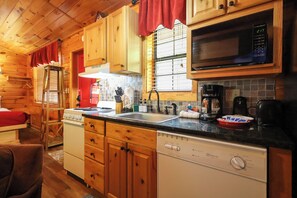 A compact kitchen with wooden cabinets, a microwave, a stove, and a dishwasher. - Hot tub, on the river, firepit, hiking trails! (Sevierville)
