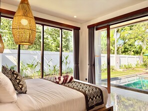 A bedroom with a large bed, a view of a swimming pool, and a balcony with plants.