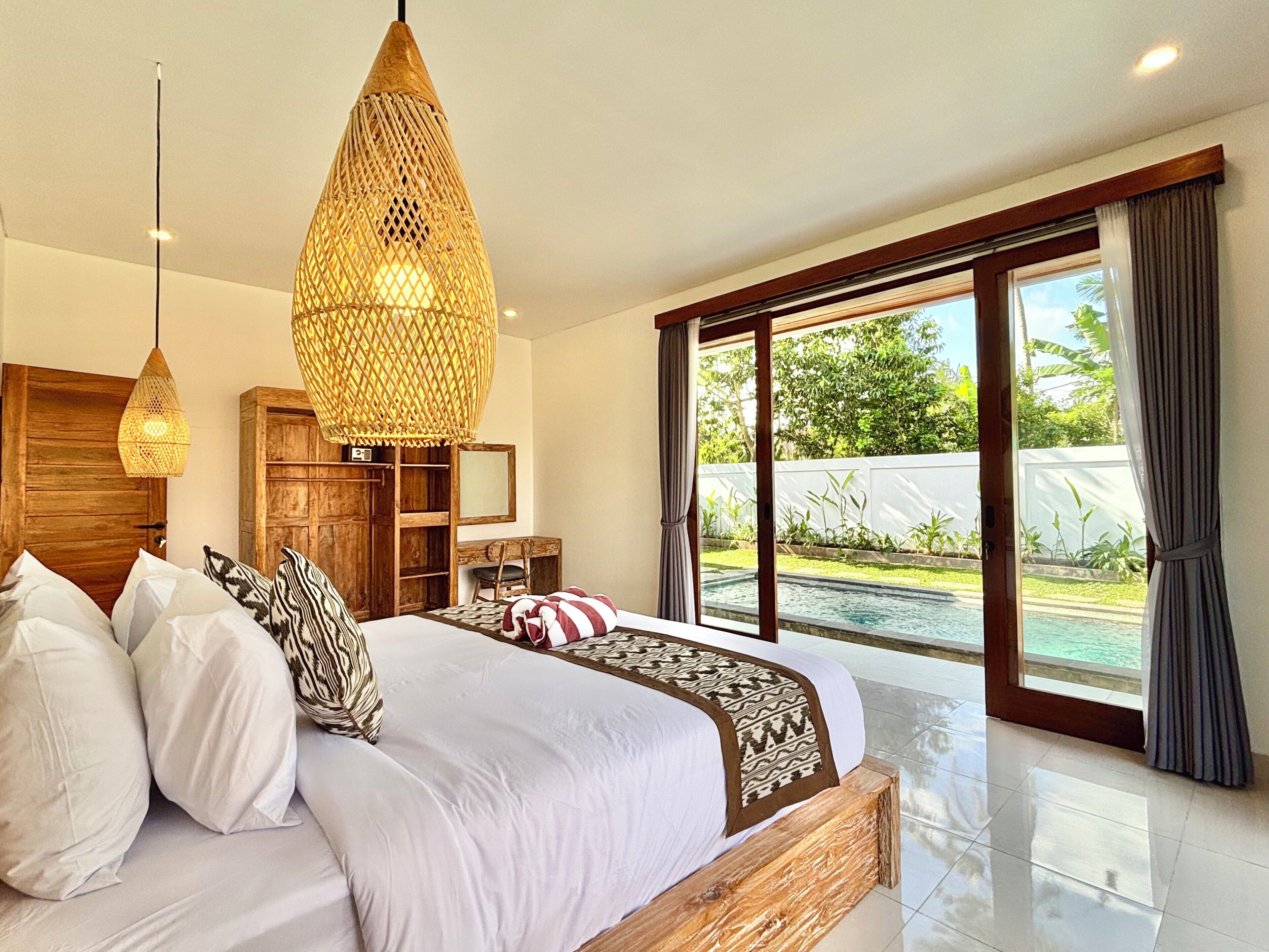 A bedroom with a large bed, wooden headboard, and two hanging light fixtures.