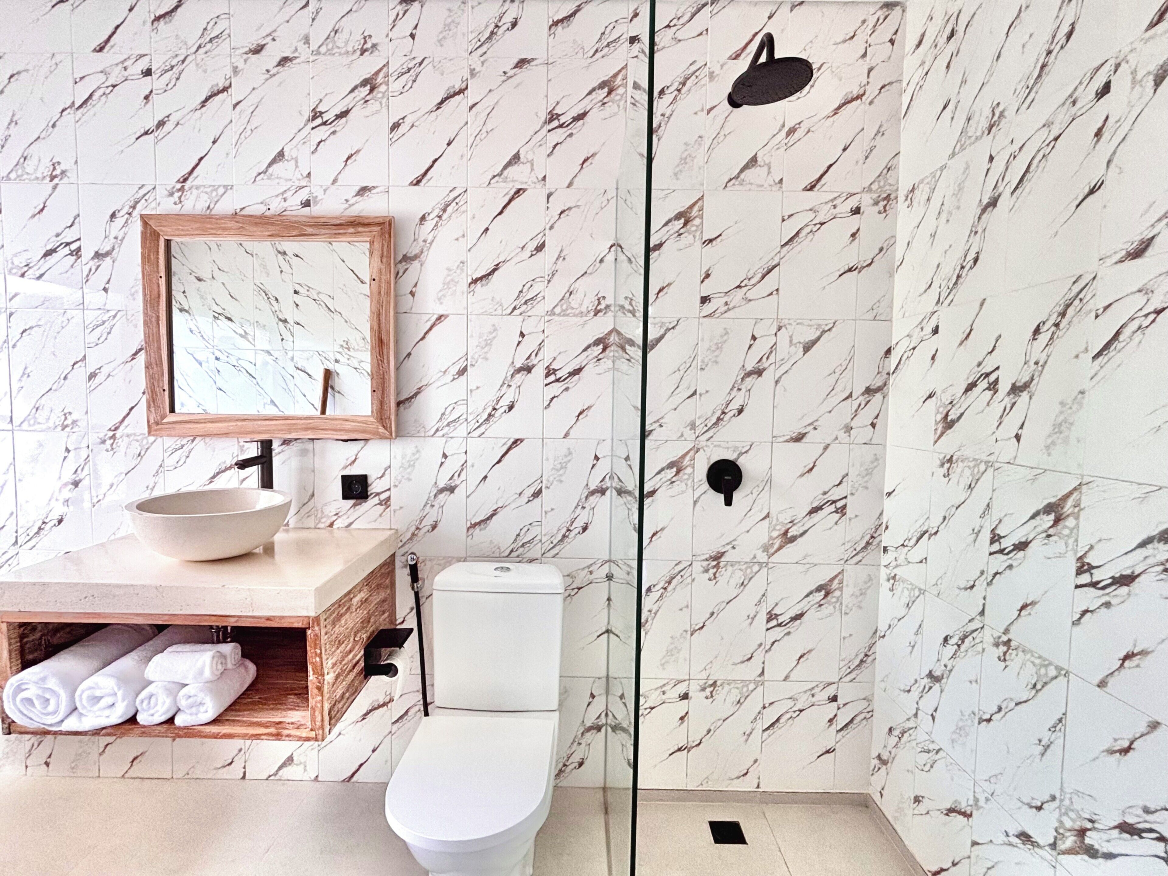 Ein Badezimmer mit einer Wand im Marmor-Muster, einem hölzernen Waschtisch, einer weißen Spüle und einer Toilette.
