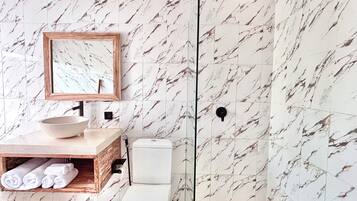 Ein Badezimmer mit einer Wand im Marmor-Muster, einem hölzernen Waschtisch, einer weißen Spüle und einer Toilette.