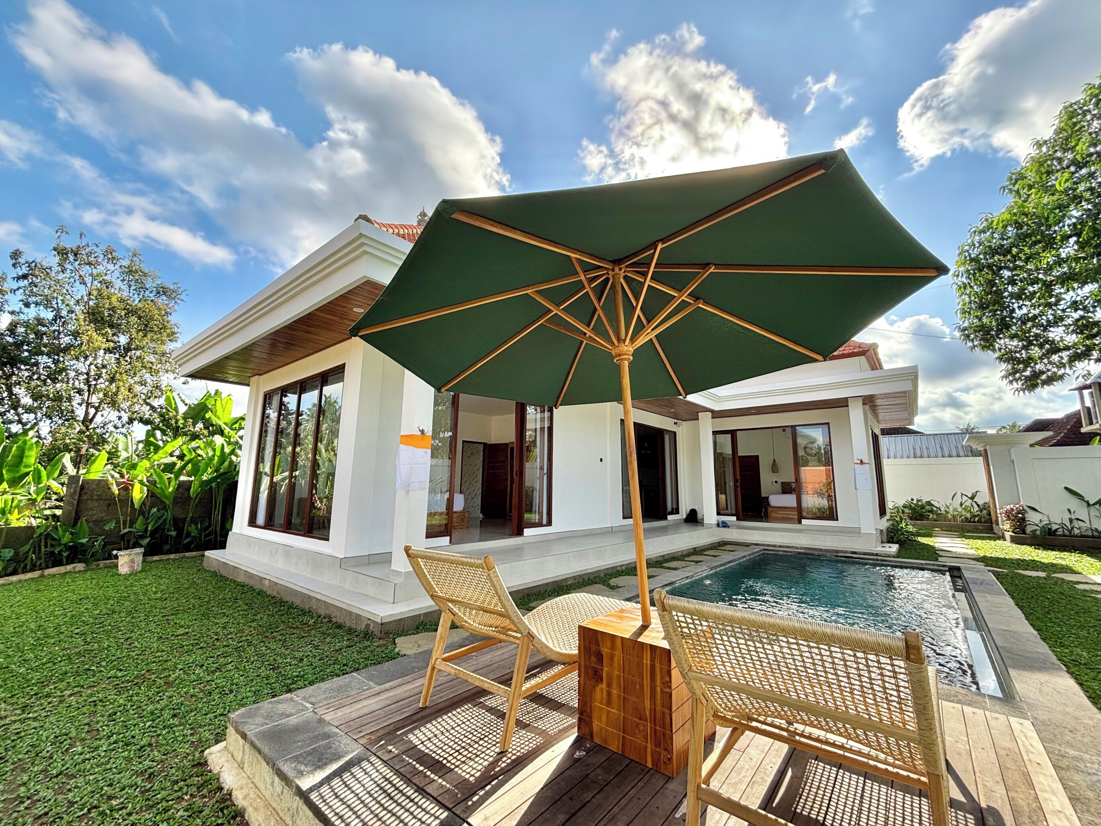 A poolside area with a wooden deck, two wicker chairs, and a large umbrella.