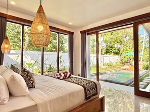 Camera da letto con un ampio letto, due lampade a sospensione e vista su piscina e giardino.