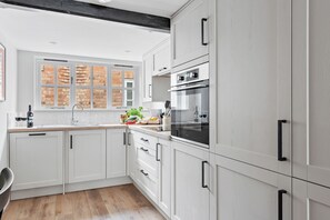Moderni keittiö, jossa on valkoiset kaapit, sisäänrakennettu uuni ja ikkuna, josta avautuu näkymä tiiliseinälle.