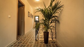 Un pasillo con suelo estampado, una planta en maceta, una puerta y una lámpara fijada a la pared.