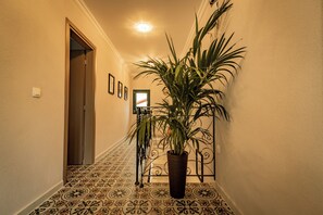 A hallway with patterned flooring, a potted plant, a door, and a wall-mounted light fixture.