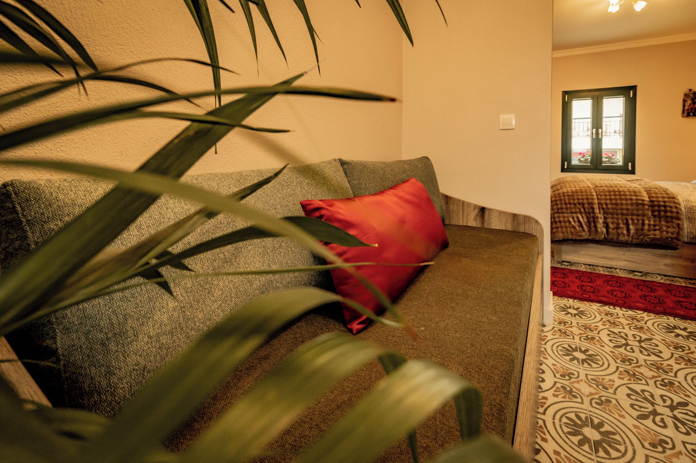Una habitación con sofá, almohada roja, alfombra estampada y ventana con vistas.