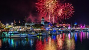 A waterfront marina with boats docked, buildings with lights, and fireworks in the sky. - NEW! Beachwalk Bliss~5 Min to Beach~Pool~Dog Friendly (Fort Walton Beach)