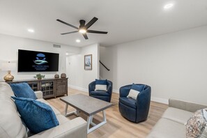 Ein modernes Wohnzimmer mit Fernseher, Deckenventilator und einer blauen Couch mit Kissen.