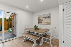 Un comedor con mesa de madera y bancos, un cuadro en la pared y un ventanal corredero que da al exterior.