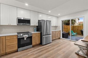 A modern kitchen with stainless steel appliances, wooden cabinets, and a sliding glass door to a patio area. - NEW! Beachwalk Bliss~5 Min to Beach~Pool~Dog Friendly (Fort Walton Beach)