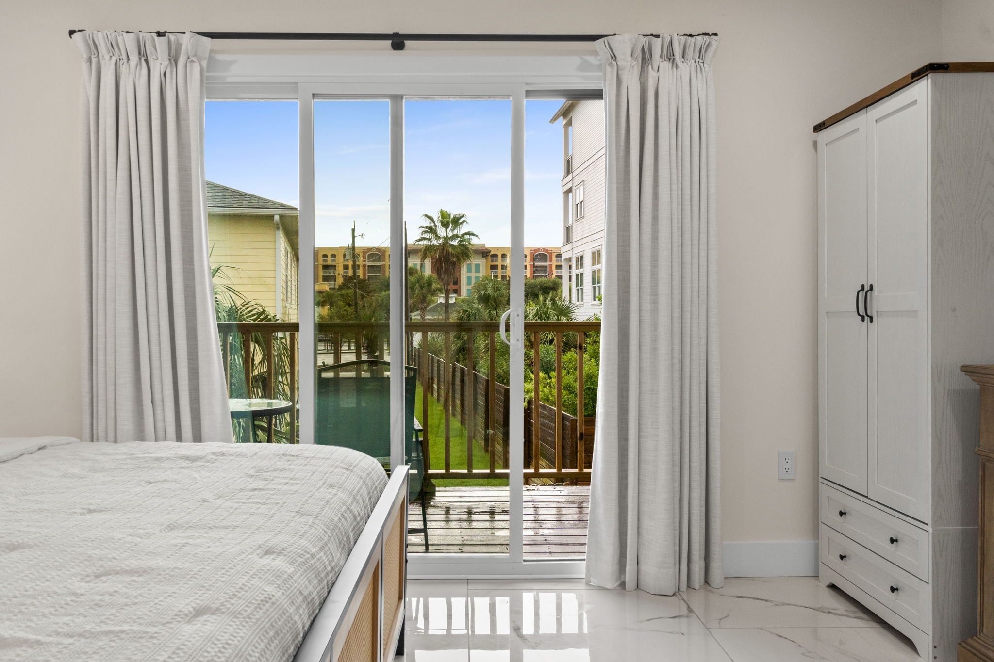 A bedroom with a bed, a wardrobe, and a balcony with a view of buildings and greenery.