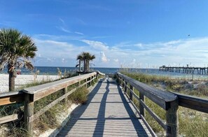 A wooden boardwalk leading to a beach with palm trees and a pier in the background. - NEW! Beachwalk Bliss~5 Min to Beach~Pool~Dog Friendly (Fort Walton Beach)