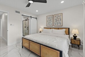 Ein Schlafzimmer mit einem Bett, zwei Nachttischen, einem Deckenventilator und Kunstwerken an der Wand.