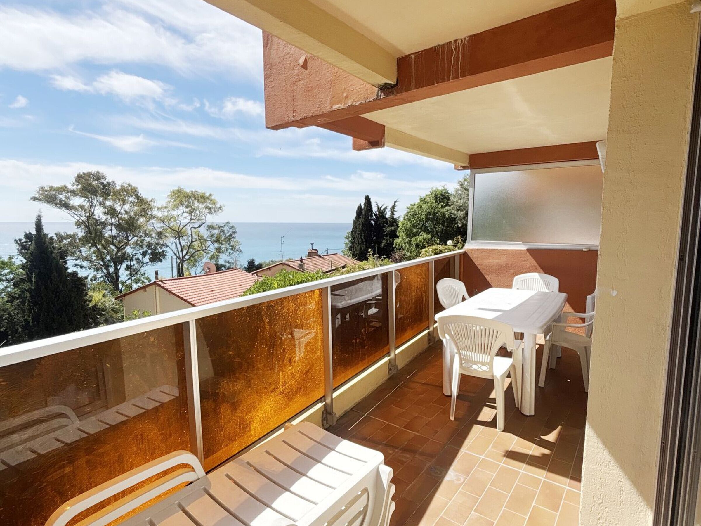 A balcony with a table and chairs, overlooking a coastal view with houses and trees.