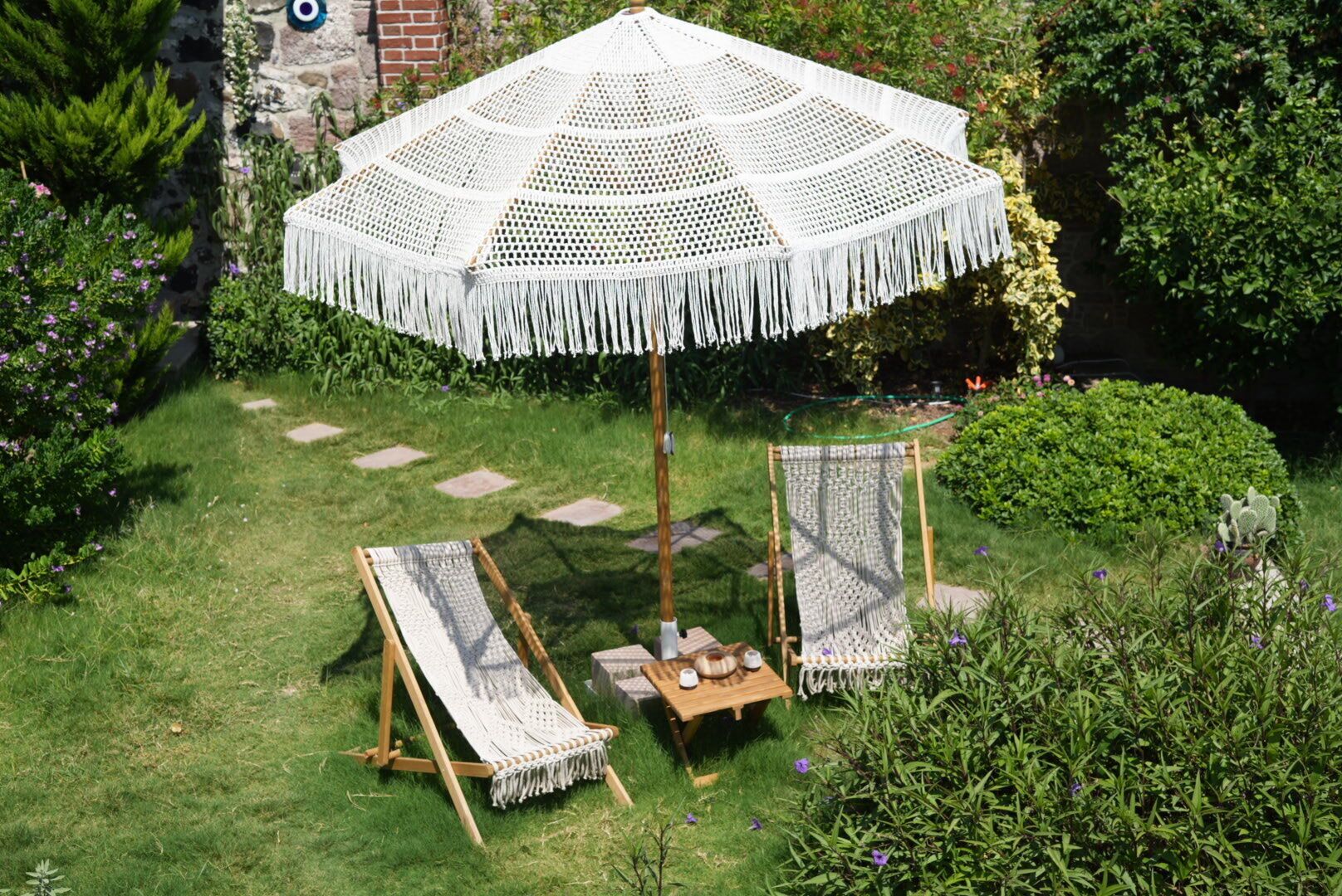 A garden with a large white umbrella, two wooden chairs, and a small table with a cup and saucer.