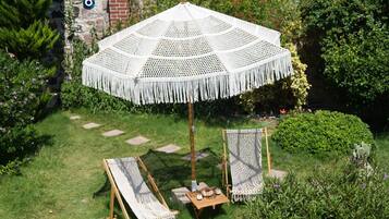 A garden with a large white umbrella, two wooden chairs, and a small table with a cup and saucer.