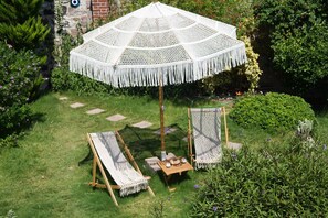 Ein Garten mit einem großen weißen Sonnenschirm, zwei Holzstühlen und einem kleinen Tisch mit Tasse und Untertasse.