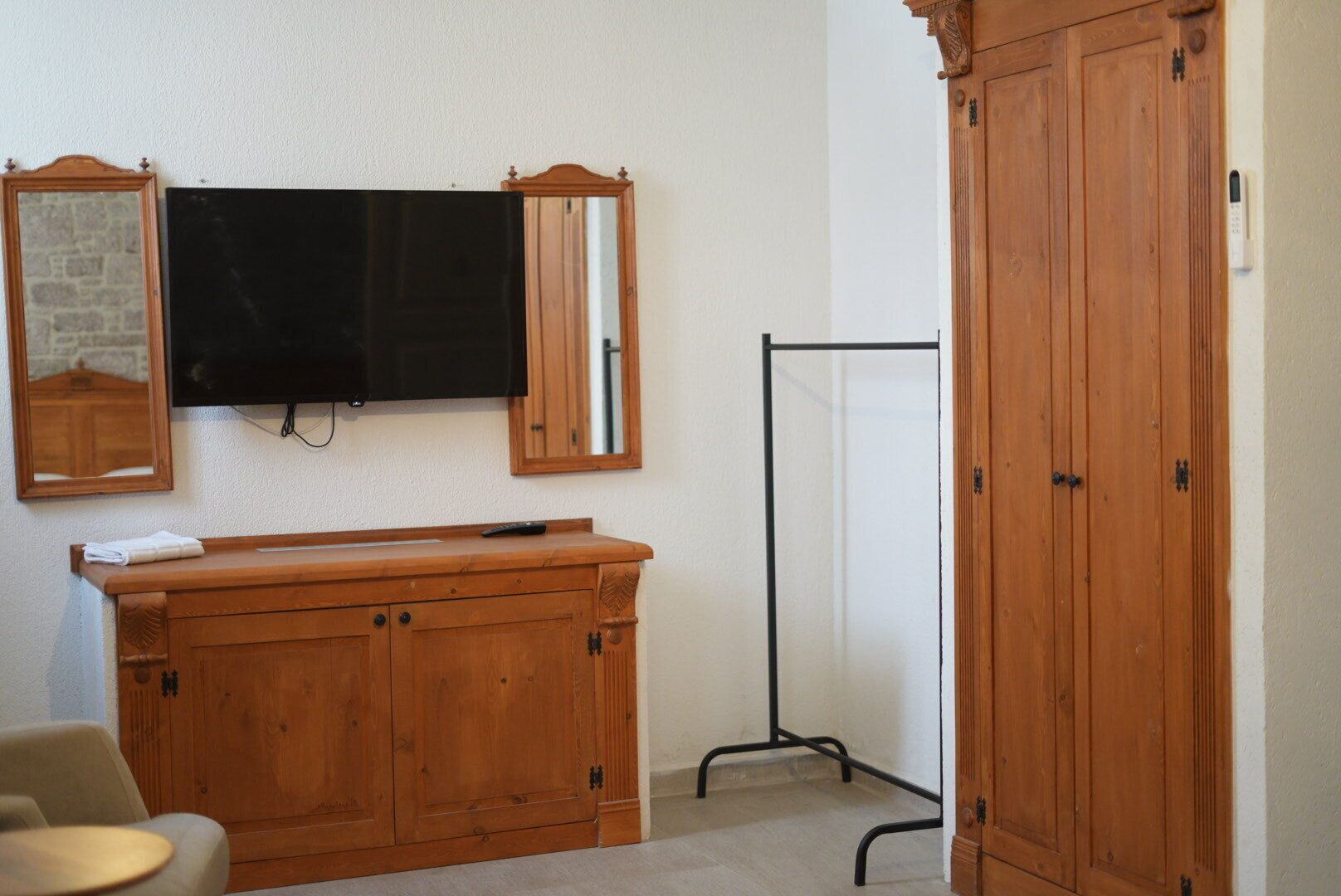 A room with a wooden cabinet, a television mounted on the wall, a mirror, and a wardrobe.