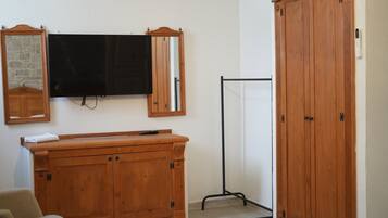 A room with a wooden cabinet, a television mounted on the wall, a mirror, and a wardrobe.