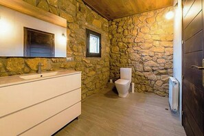 A bathroom with a stone wall, a white sink, a toilet, and a wooden door. - Designed 16th-century farmhouse among open fields (Lérida)