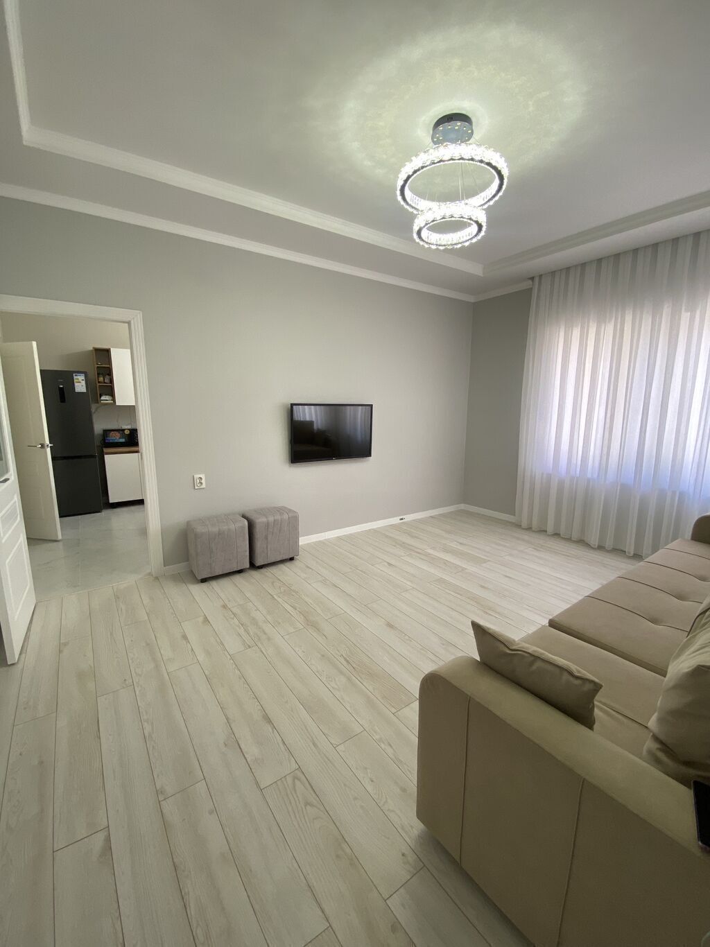 A modern living room with a flat-screen TV, a sofa, a dining area with a refrigerator, and a kitchen.