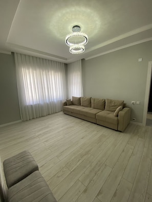 A living room with a beige sofa, a wooden floor, and a modern chandelier.
