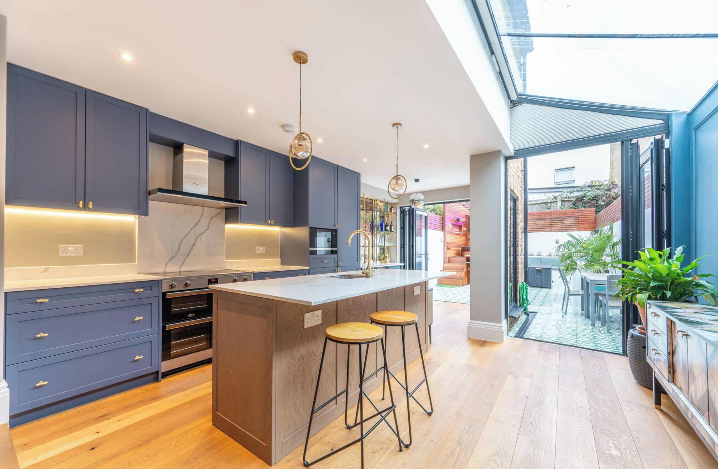 A modern kitchen with a central island, built-in ovens, and a large window overlooking a garden.