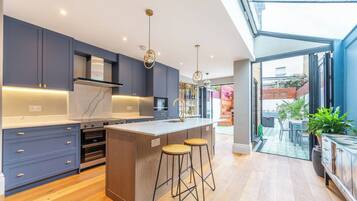 A modern kitchen with a central island, built-in ovens, and a large window overlooking a garden.