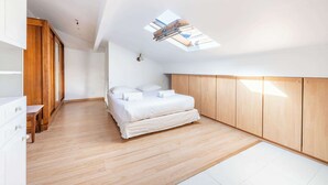 Quarto moderno com claraboia, piso de madeira e cama com roupa de cama branca.