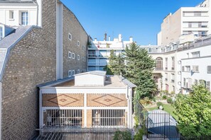 A multi-story building with a stone facade, a balcony with metal railings, and a small garden area with trees and shrubs. - Bright & Central Duplex - Near the Eiffel Tower (Paris)
