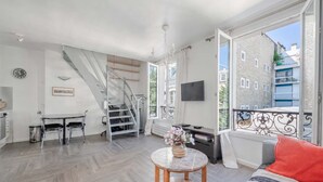 Um espaço de estar moderno com escada, área de refeições, sofá com almofada e televisão na parede.