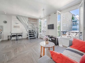 A modern living space with a staircase, a dining area, a sofa with a throw pillow, and a TV mounted on the wall. - Bright & Central Duplex - Near the Eiffel Tower (Paris)