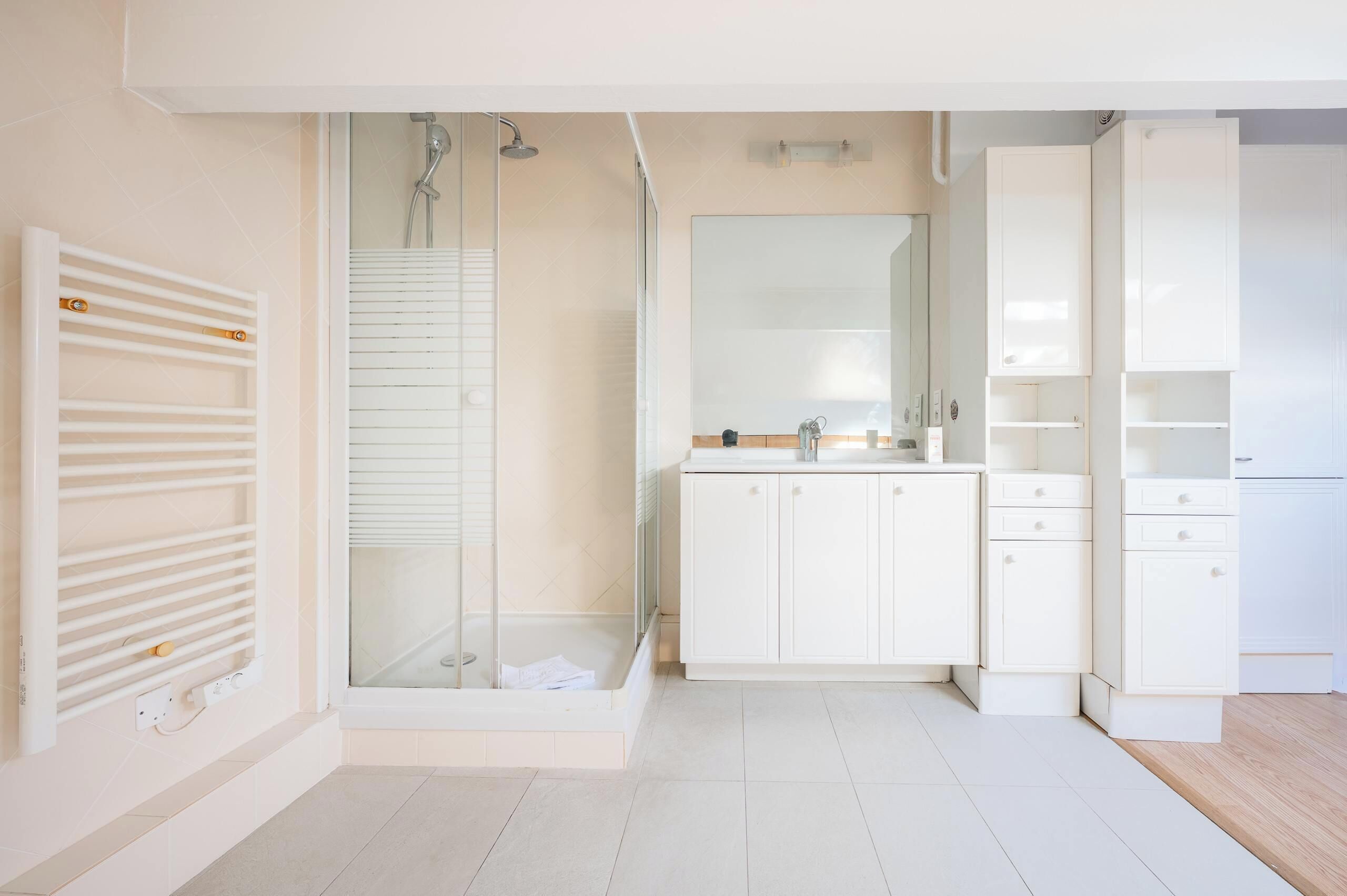 Une salle de bain moderne avec une douche à parois de verre, un meuble-lavabo blanc avec un miroir et un plancher en bois.