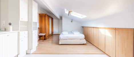 Un dormitorio con cama, armario de madera y tragaluz.