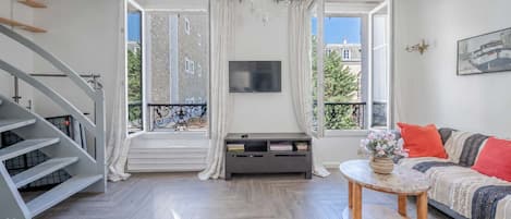 A modern living room with a staircase, a flat-screen TV, a sofa with cushions, and a small round table.