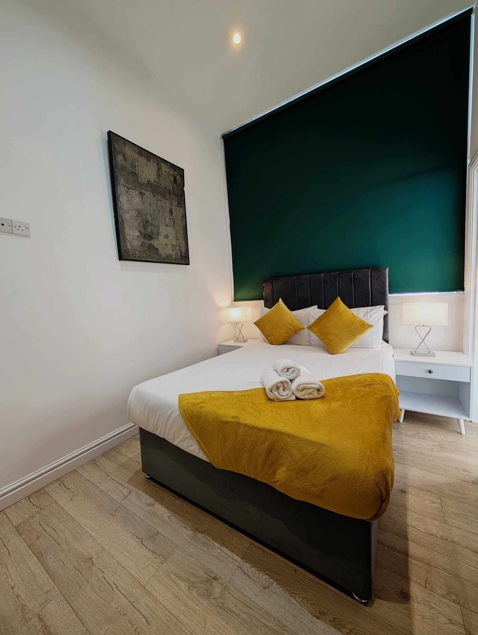 A modern bedroom with a bed, bedside tables, and a green accent wall.